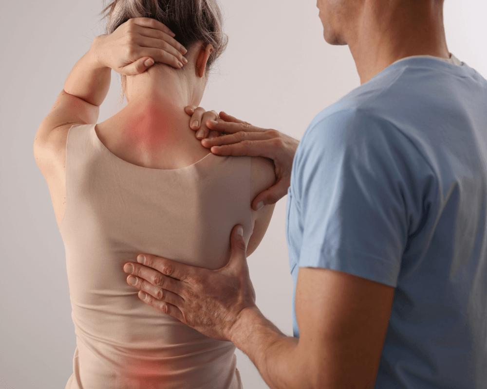 A therapist gently massages a woman's upper back, highlighting her pain area with redness on her skin, indicating discomfort.