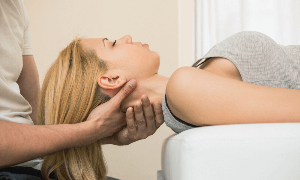 A person receiving a neck massage while laying on a treatment table, hair cascading over the edge. Soft lighting creates a calm atmosphere.