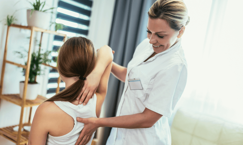 A healthcare professional assists a patient with a shoulder stretch in a bright, calming therapy room filled with plants.